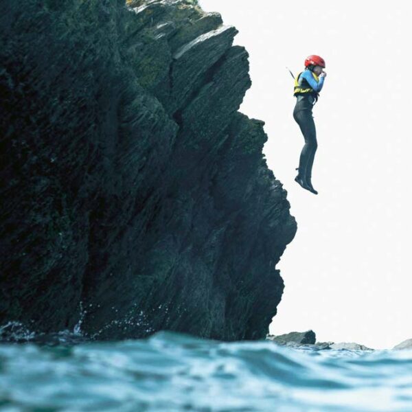 Girl in wetsuit and helmet jumping into the sea from rocks