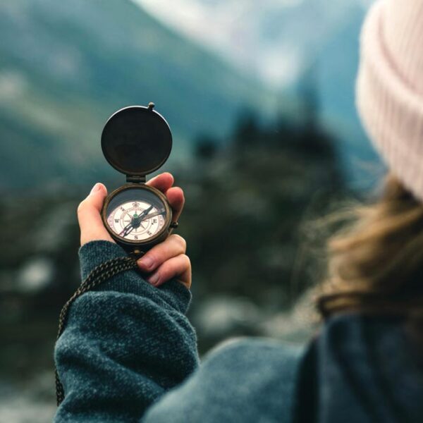 girl with hat holds a compass in mountain landscape