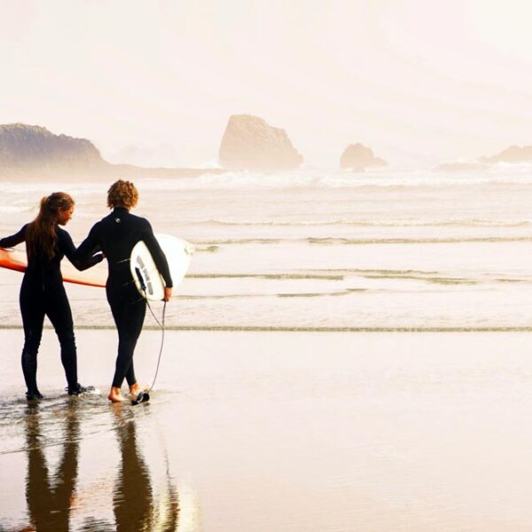 Two teenage surfers walking into the water with surfboards